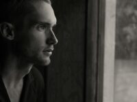 Fotografía en escala de grises de un hombre frente a un panel de cristal