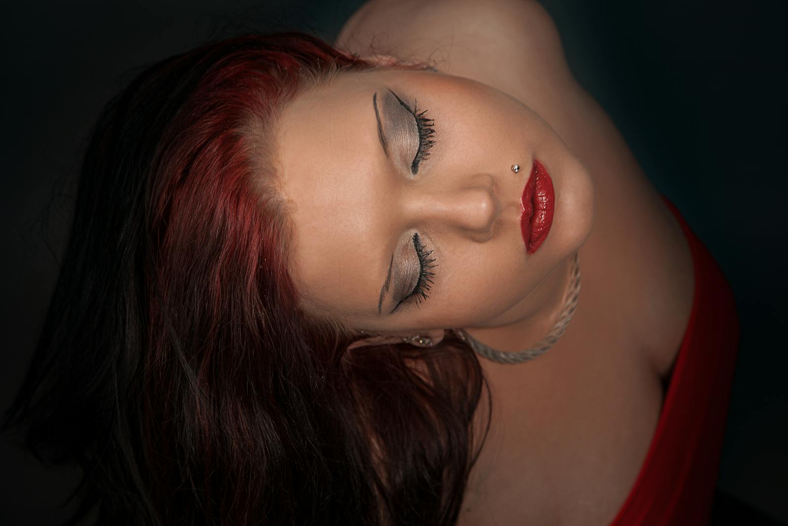 Artistic portrait of a woman with closed eyes and bold makeup in a dramatic pose.
