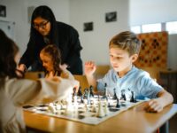 Niños pequeños jugando ajedrez bajo la supervisión de un adulto en un aula.