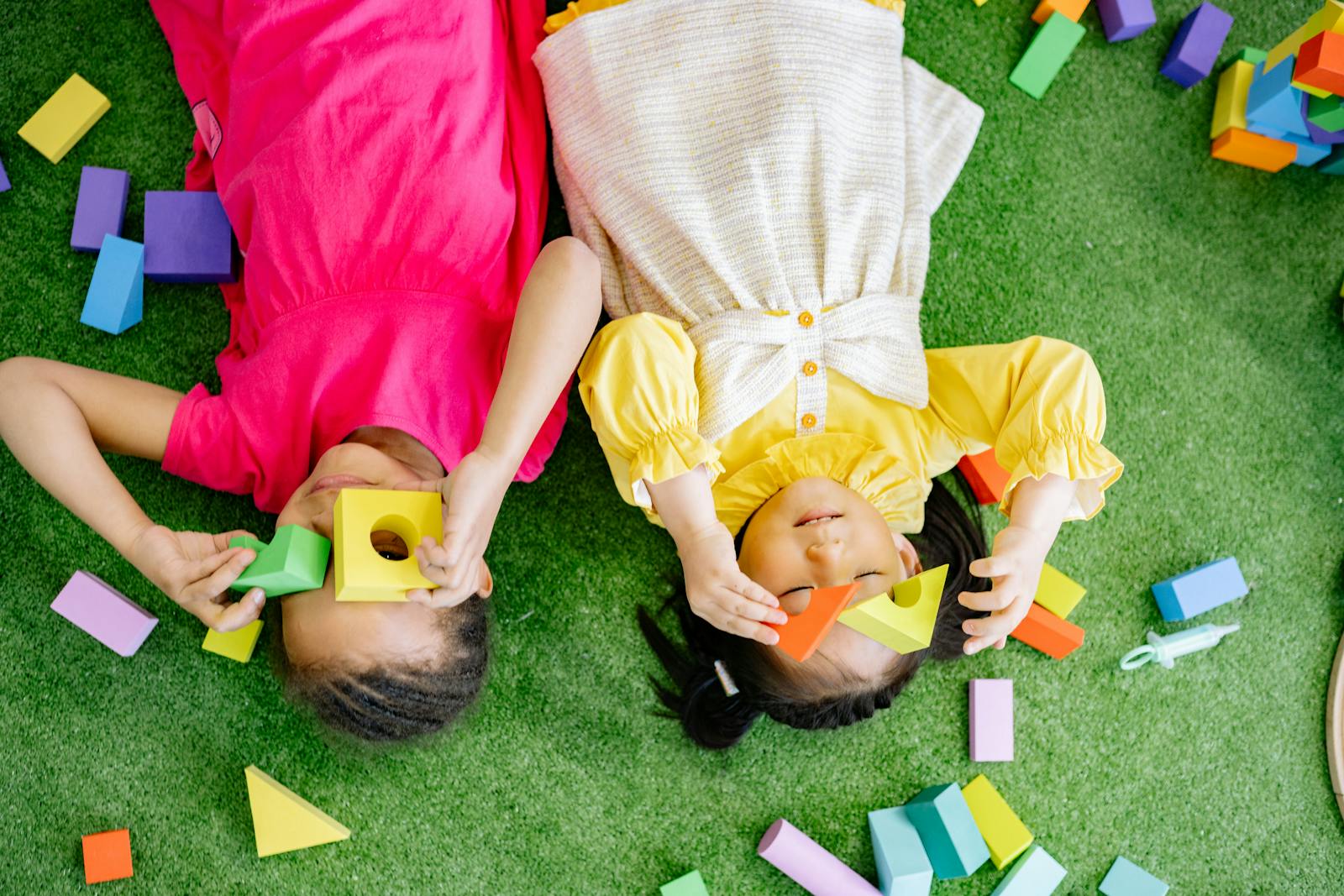 Dos niños alegres jugando con bloques de madera de colores sobre una superficie verde en el interior.