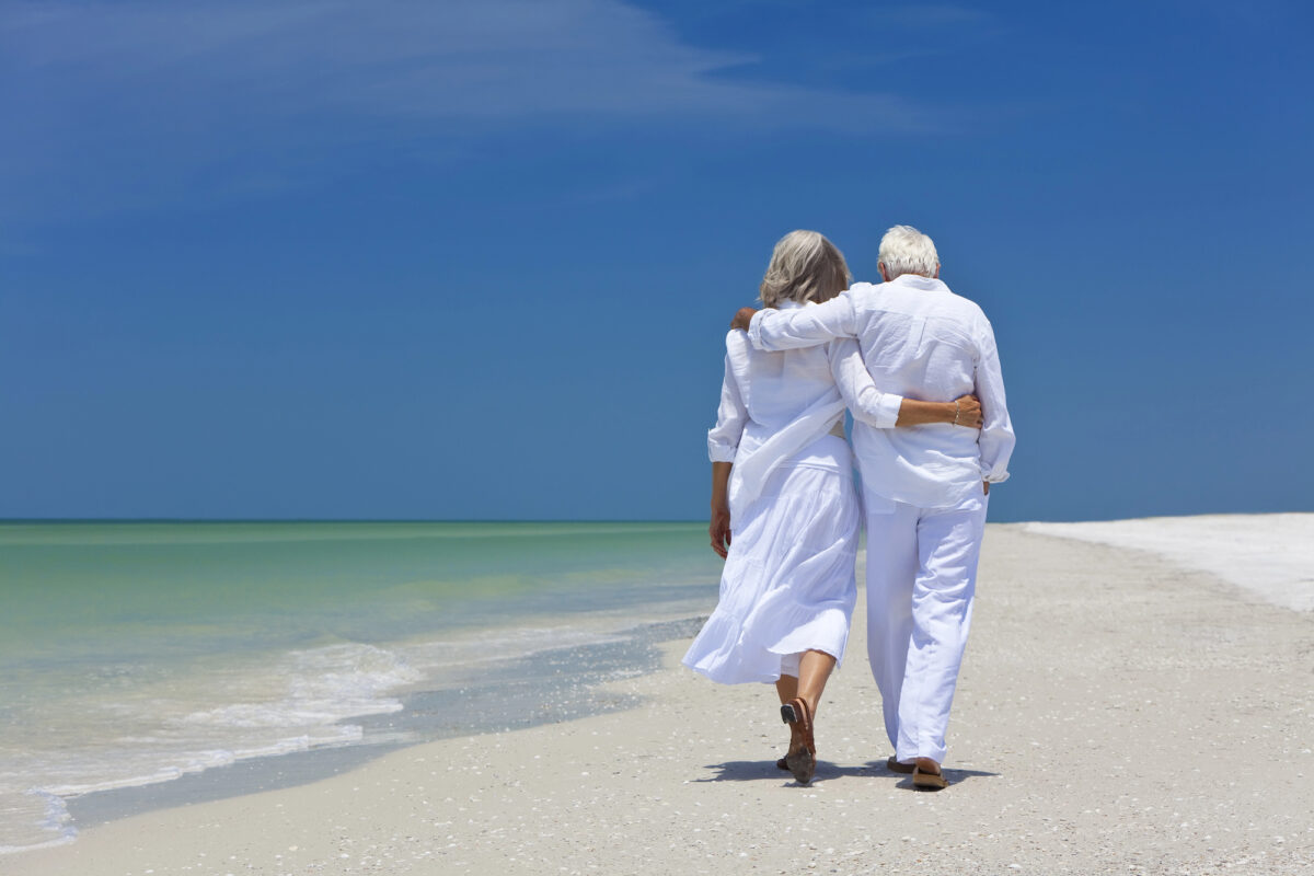 Pareja de adultos mayores camina al borde de la playa.