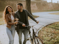 Guapo joven pareja caminando con bicicleta en el parque de otoño